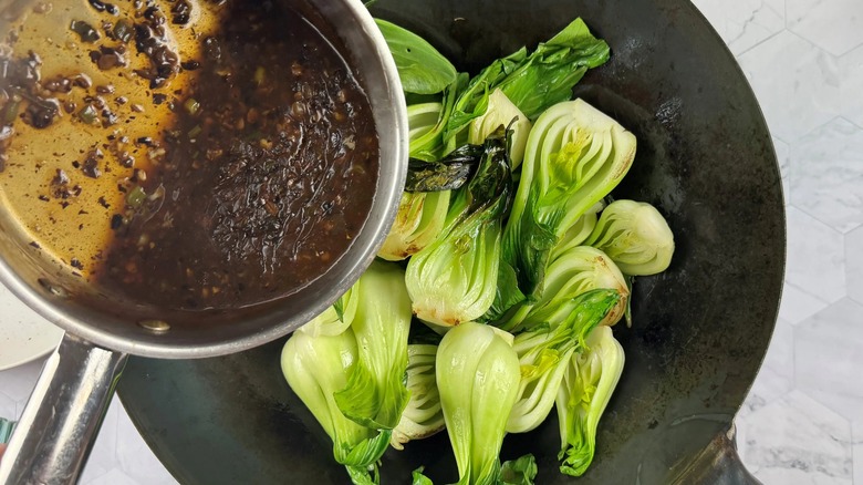 hand pouring black sauce onto cooked bok choy