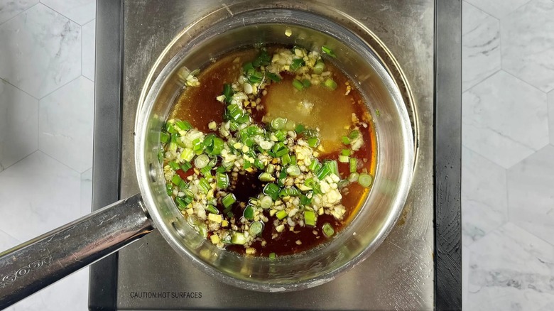 green onions, garlic, and ginger in a frying pan with brown liquid