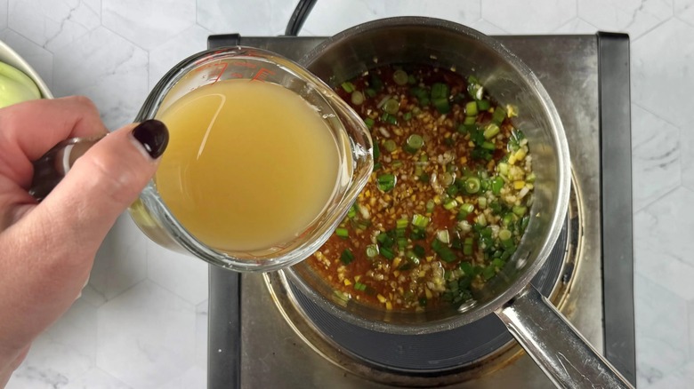 hand pouring yellow liquid into a pot of onions in liquid