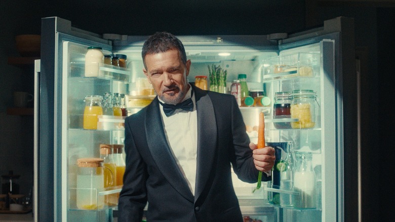 Antonio Banderas in suit in front of fridge with carrot in hand