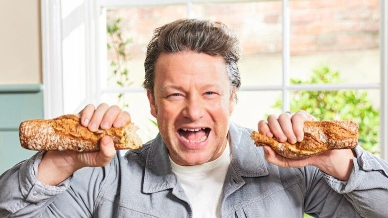 Jamie Oliver holding two pieces of baguette and staring straight ahead