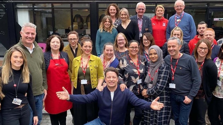 Jamie Oliver kneeling in front of a group of Jamie's Ministry of Food volunteers and staff