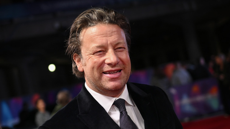 Chef Jamie Oliver in a green shirt standing in front of a graffiti-covered wall