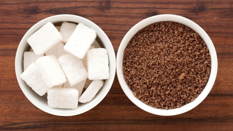 Bowl of white sugar cubes next to bowl of brown sugar on wood table