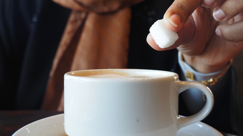 Person dropping sugar cube into coffee drink