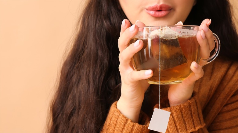 Person blowing on cup of tea with tea bag