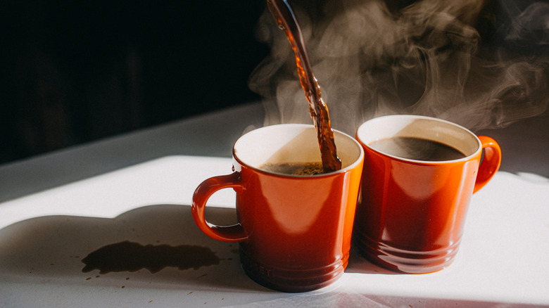 Two cups of hot coffee poured messily into red mugs.