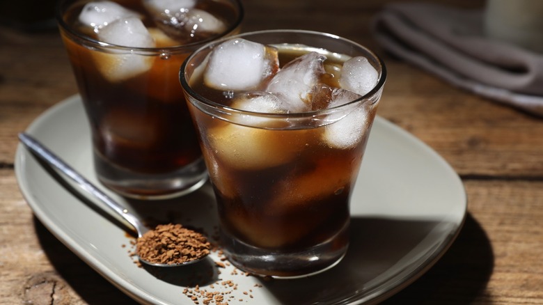 Two glasses of iced coffee with ice cubes near spoon with instant coffee