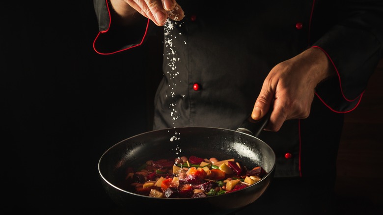 Chef salting veggies in pan