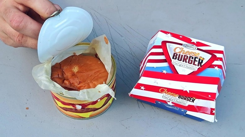 Opened canned cheeseburger can and paper container on gray table.