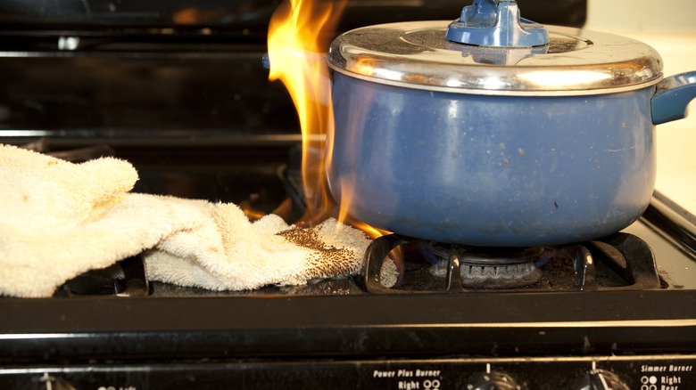 towel catching fire on a gas stove next to a blue pot