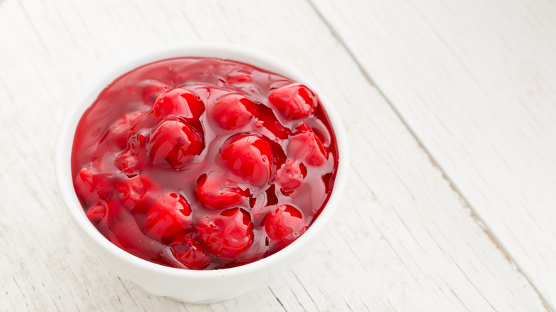 White bowl with red cherry pie filling on wood surface.