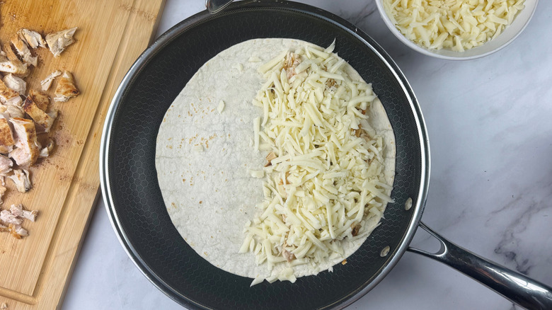 Half filled quesadilla with cheese in skillet