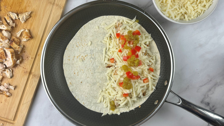 Half filled quesadilla with cheese and peppers in skillet