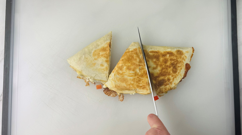 Knife slicing quesadilla on cutting board