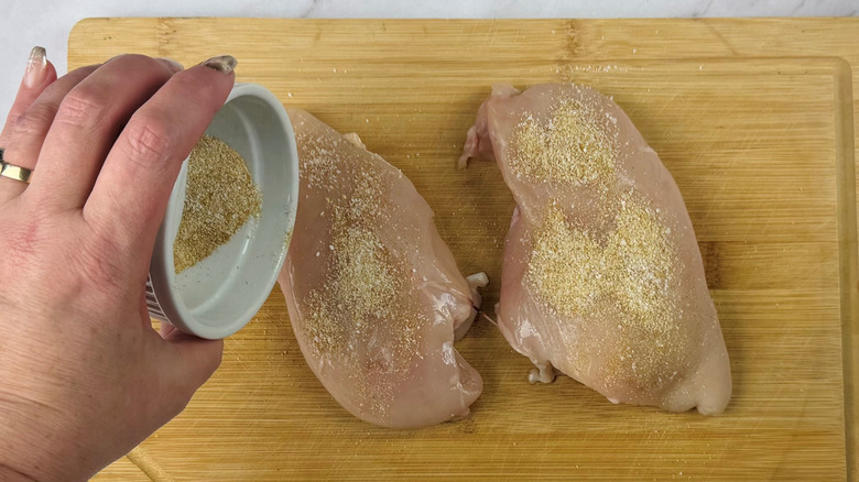 Hand pouring seasoning onto chicken breasts