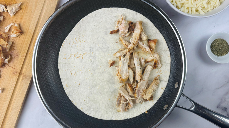 Tortilla in pan halfway covered with shredded chicken