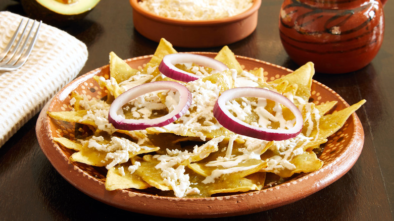 A plate of chilaquiles topped with green salsa, cheese, and onions.