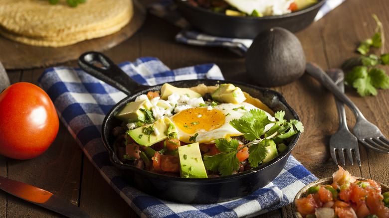 Huevos rancheros prepared in cast iron pan with colorful toppings.