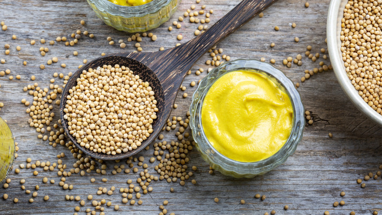 Different types of mustard and mustard seeds on a rustic wooden board.