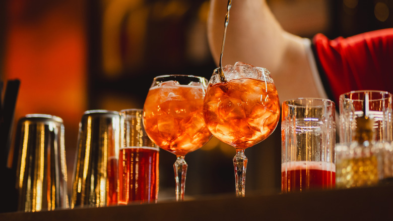 Aperol spritz cocktails on bar with bartender stirring one glass.