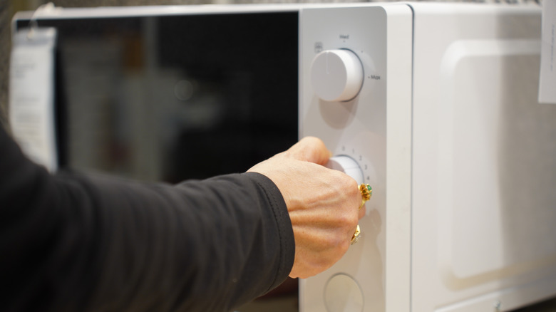 A person turning the dial on the microwave