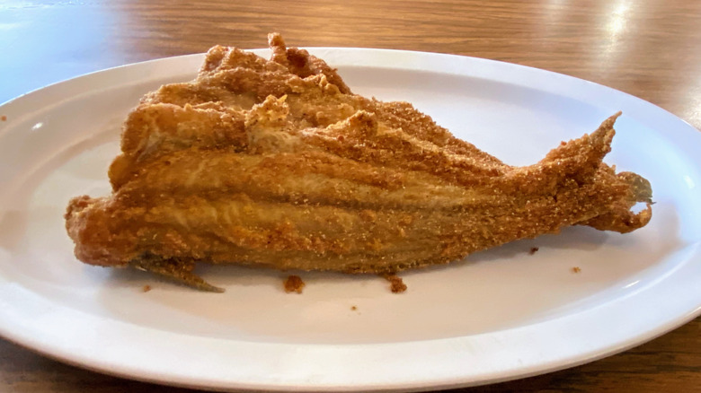 A white plate of two fried catfish filets on a wooden table