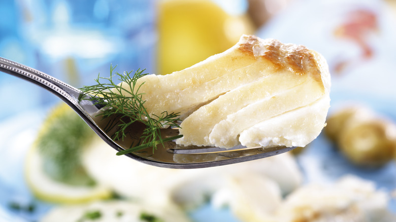 Close-up of a few flakes of cod on a silver fork, with a dish of the fish in the background