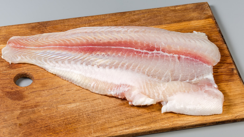 Defrosted filet of the Pangasius on a big wooden cutting board on gray background