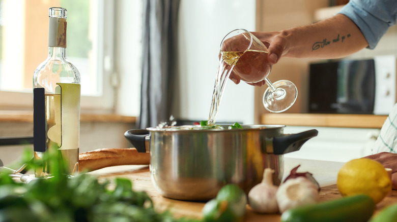 Person pouring white wine from glass into metal cooking pot.