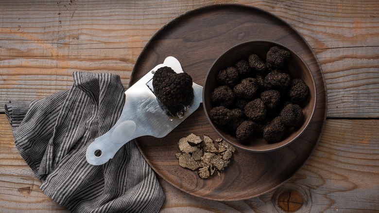 wooden bowl of black truffle, shaved truffle on wooden plate underneath