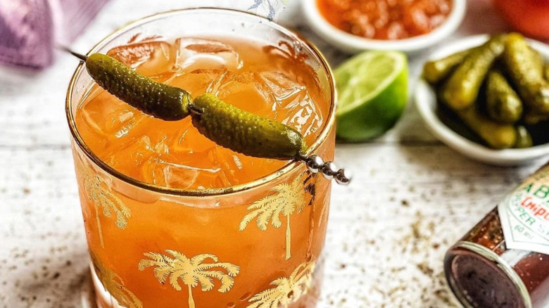 Small orange margarita cocktail with skewered cornichons.