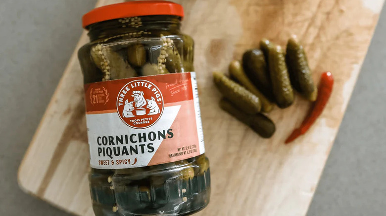 Glass jar of pickled cornichons and hot peppers.