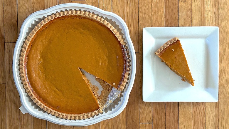 Whole and slice of Pumpkin Pie on white square plate