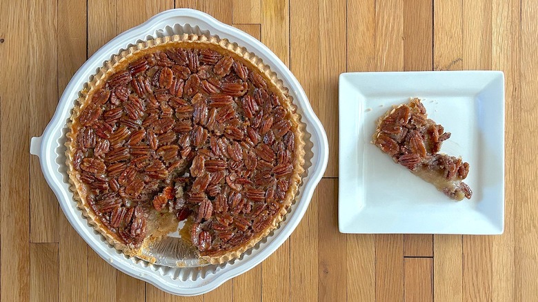 Whole and slice of Pecan Pie on white square plate