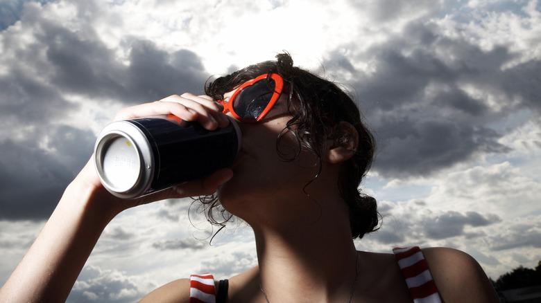 A woman with sunglasses sips from a can