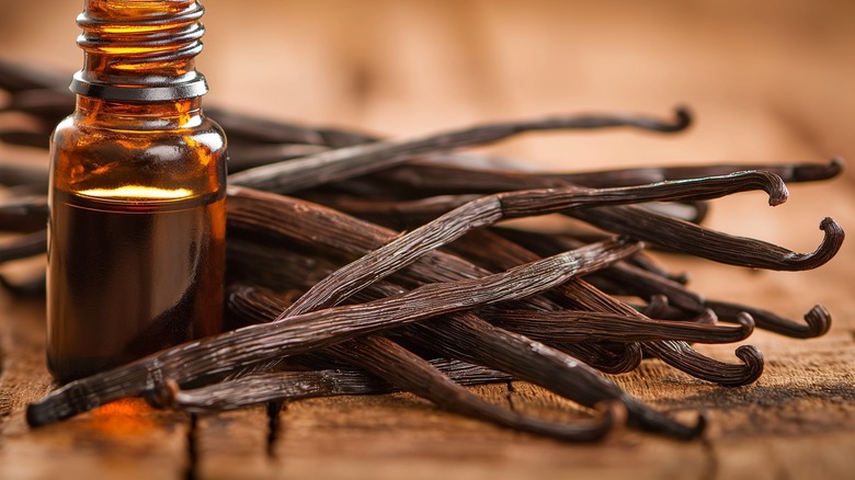 Vanilla bean pods next to a small dark brown bottle