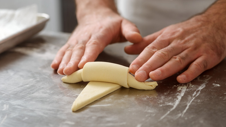 two hands rolling crescent roll dough