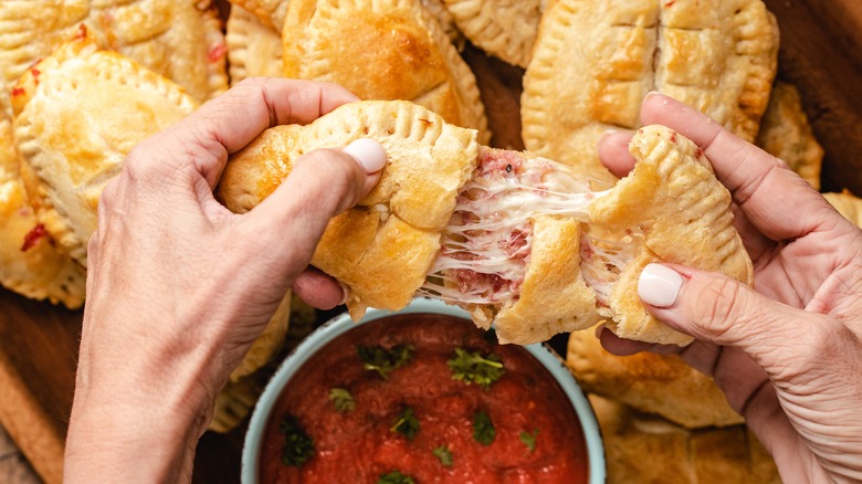 woman's hands pulling apart a pizza-shaped roll with meat and cheese filling