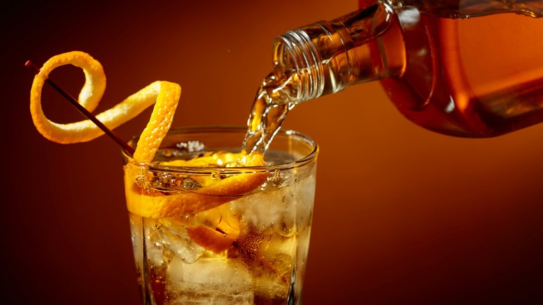 Whisky being poured into old fashioned cocktail with orange peel garnish