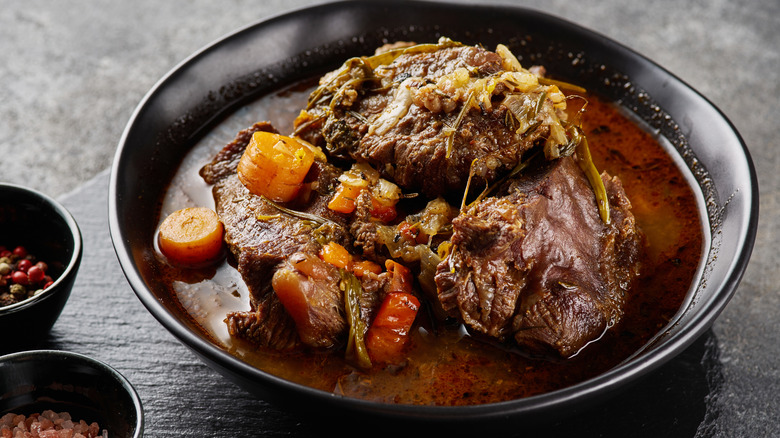 traditional german braised beef cheeks in brown red wine sauce with herbs as closeup in black plate