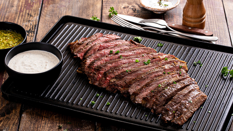 Grilled flank steak with chimichurri and horseradish sauce on a grill pan on wooden table