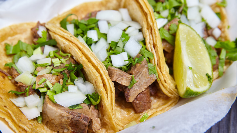 Lengua chow beef tongue 3 street tacos Mexican with cilantro, onions and lime wedge