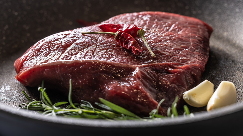 Raw beef rump steak in a pan with garlic chili pepper and rosemary