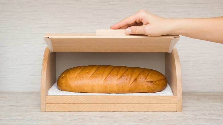 Hand opening or closing wooden breadbox with white bread inside on table top at home kitchen.