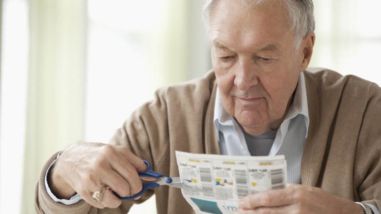 Senior man in cardigan clipping coupons with scissors.