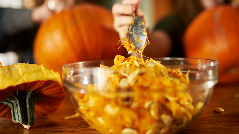 Scooping out pumpkin guts and seeds into clear glass bowl