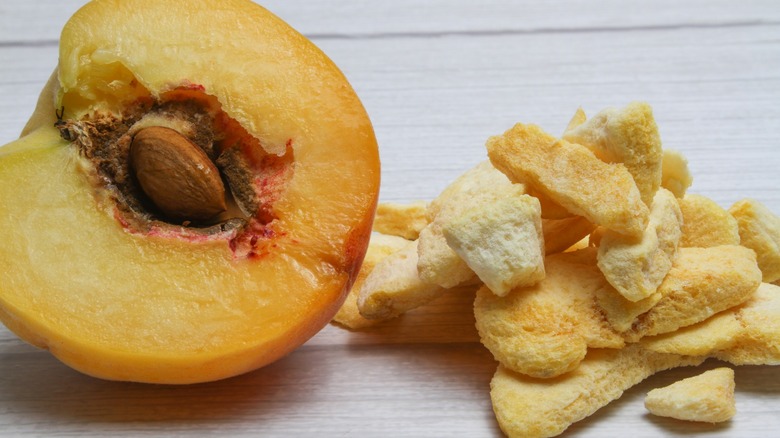 Half a peach next to freeze-dried peach pieces on white table