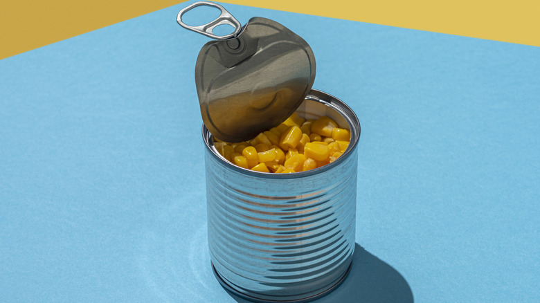 An opened can of corn with the lid peeled back on a blue and yellow background.