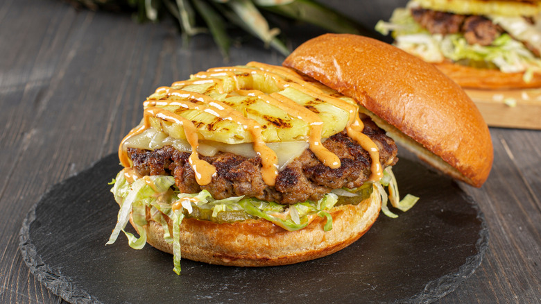 Hamburger with open bun and slice of grilled pineapple.